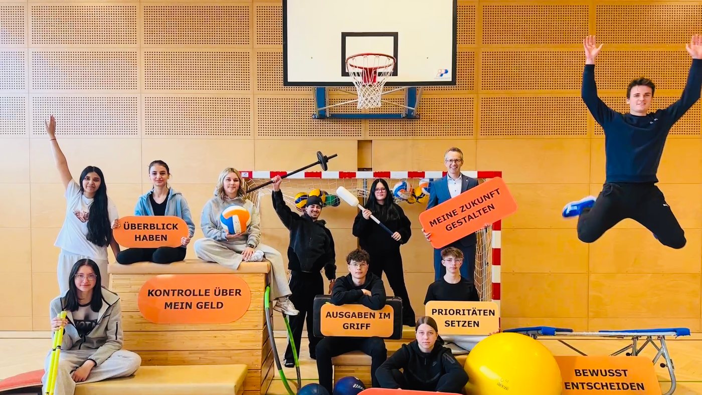 Jugendliche in der Turnhalle mit Schildern zu Finanzthemen